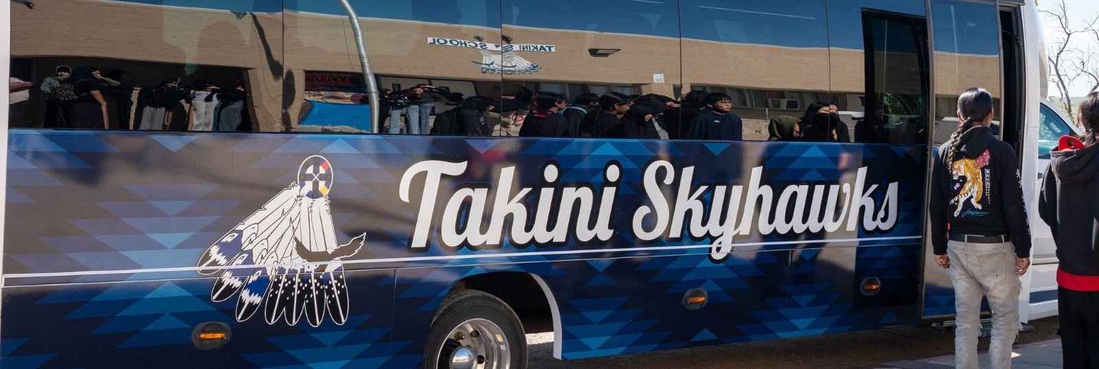 A bright Takini Skyhawks bus, showcasing the school's colors and logo, is shown parked and waiting for passengers.