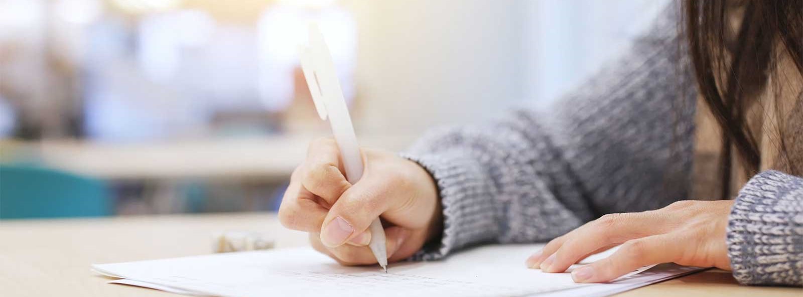 A student writes on paper with a pen, focused on their task.