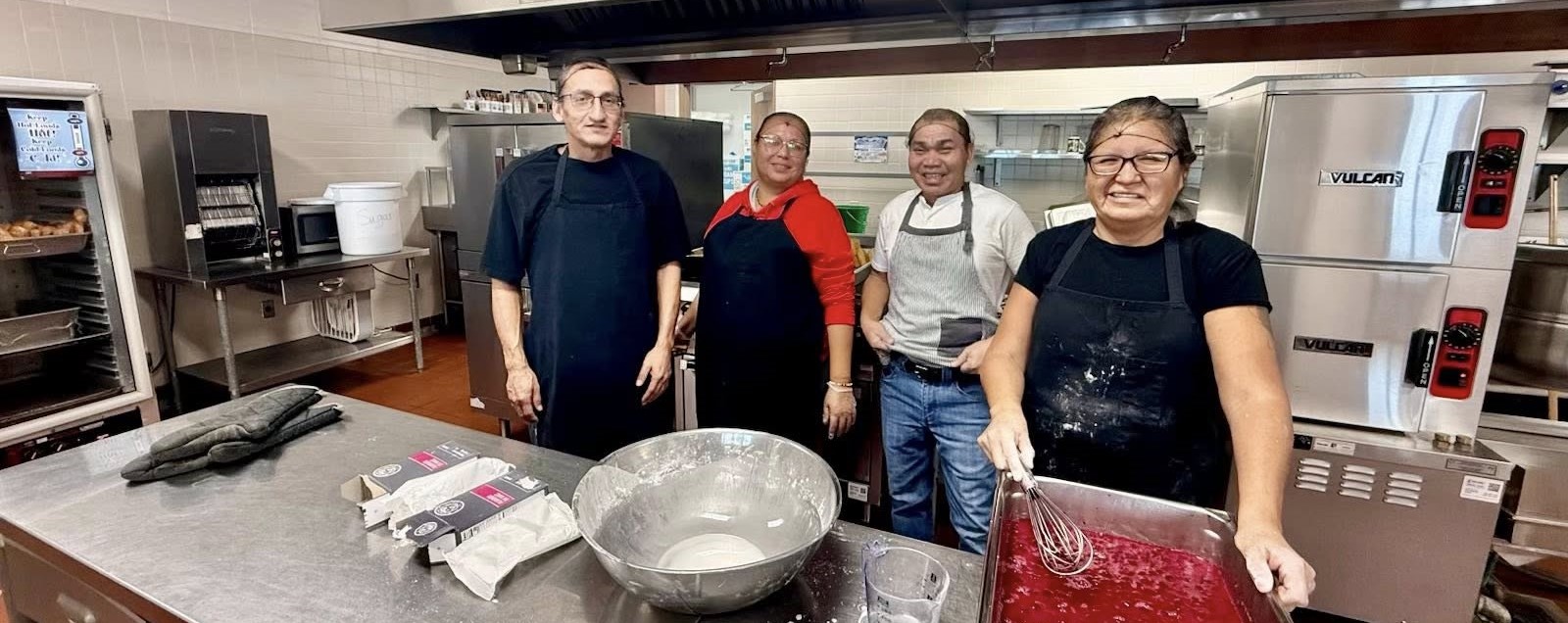 The members of the school food services team are in the kitchen, working together to prepare and serve meals for students.