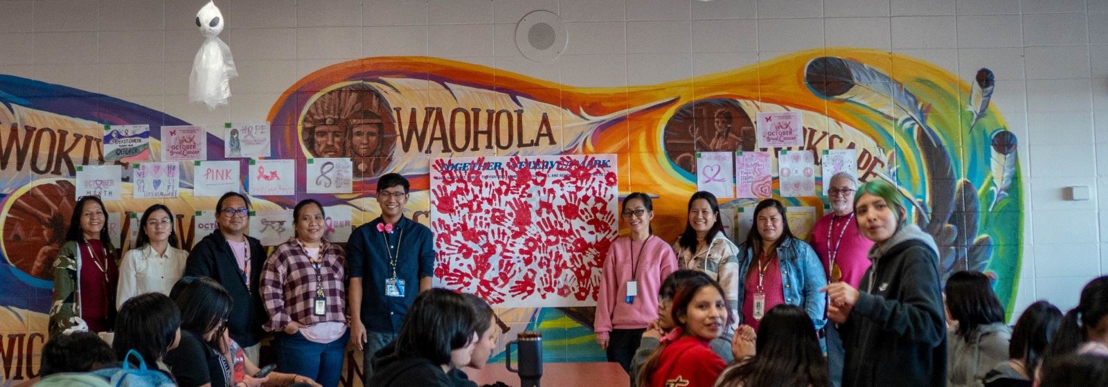 Several students stand together in front of a colorful mural, smiling and enjoying the artwork.