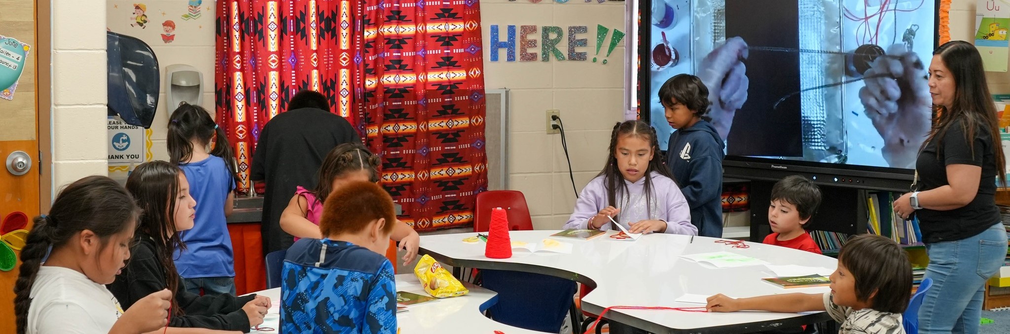 Children gathered at tables in a classroom, focused on their work during a lively school class session.