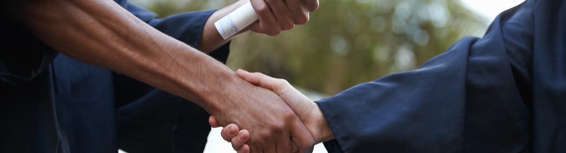 Two graduates in gowns shaking hands.