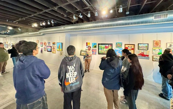 Students at Suzi Cappa Art Center admire art while listening to a speaker holding a piece in an art gallery.