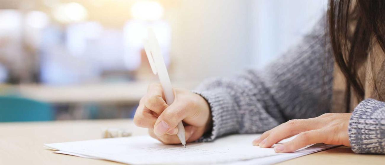 A student writes on paper with a pen, focused on their task.